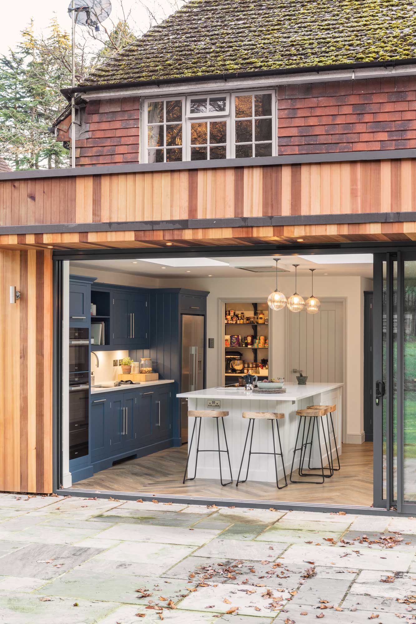 External view of navy Shaker kitchen with white kitchen island seen through open large glass sliding door