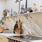 Marble splashback against white kitchen works tops and beige cabinetry containing a cooker