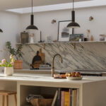 Beige kitchen island with white worktop in front of a black and white marble splashback