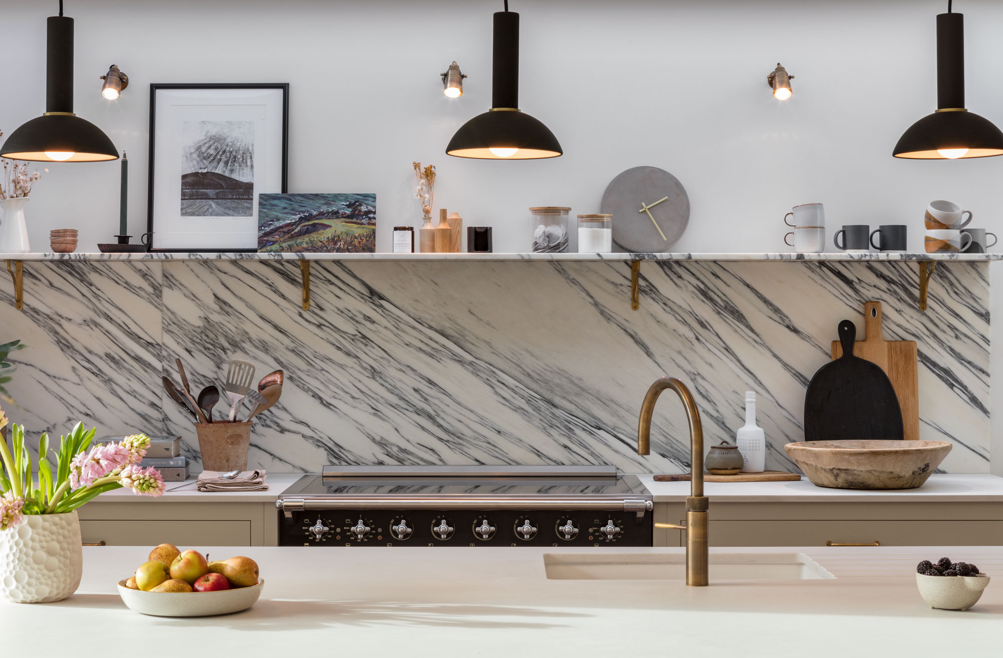 Black and white marble splashback against white worktops and white kitchen island featuring integrated sink with brass tap