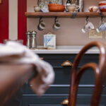 Teal kitchen cabinetry with brass handles and white worktop with overhead shelving
