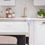 White Shaker kitchen cabinetry with brass handles and white worktop with brass tap against herringbone tiled splashback