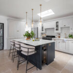 Dark Shaker kitchen island with white worktop and cream and black stools overlooking white Shaker kitchen cabinetry