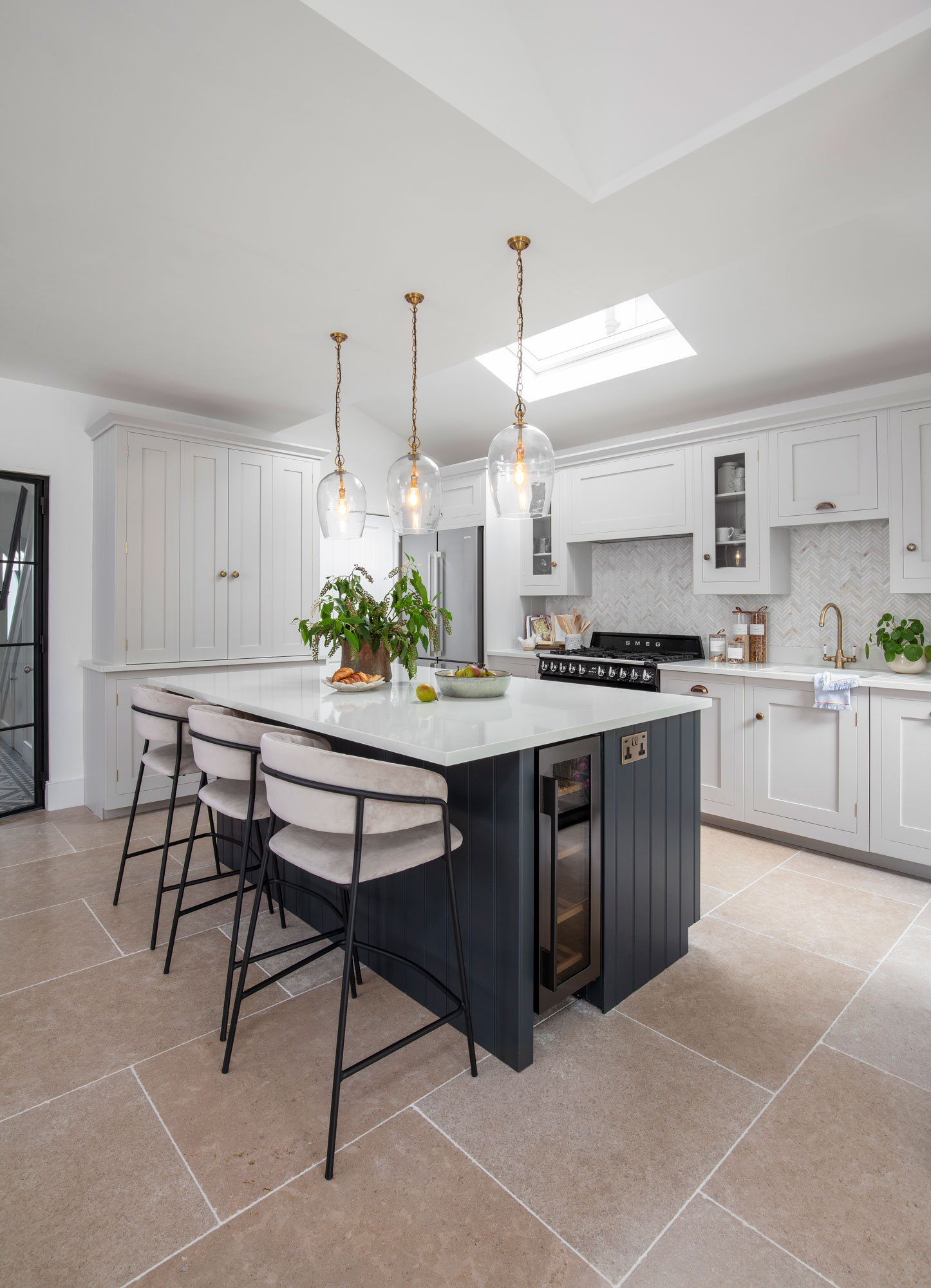Dark Shaker kitchen island with white worktop and cream and black stools overlooking white Shaker kitchen cabinetry