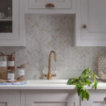 White Shaker kitchen cabinetry with white worktop and beige herringbone tiled splashback