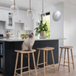Dark Shaker kitchen island with white worktop and cream and black stools overlooking white Shaker kitchen cabinetry