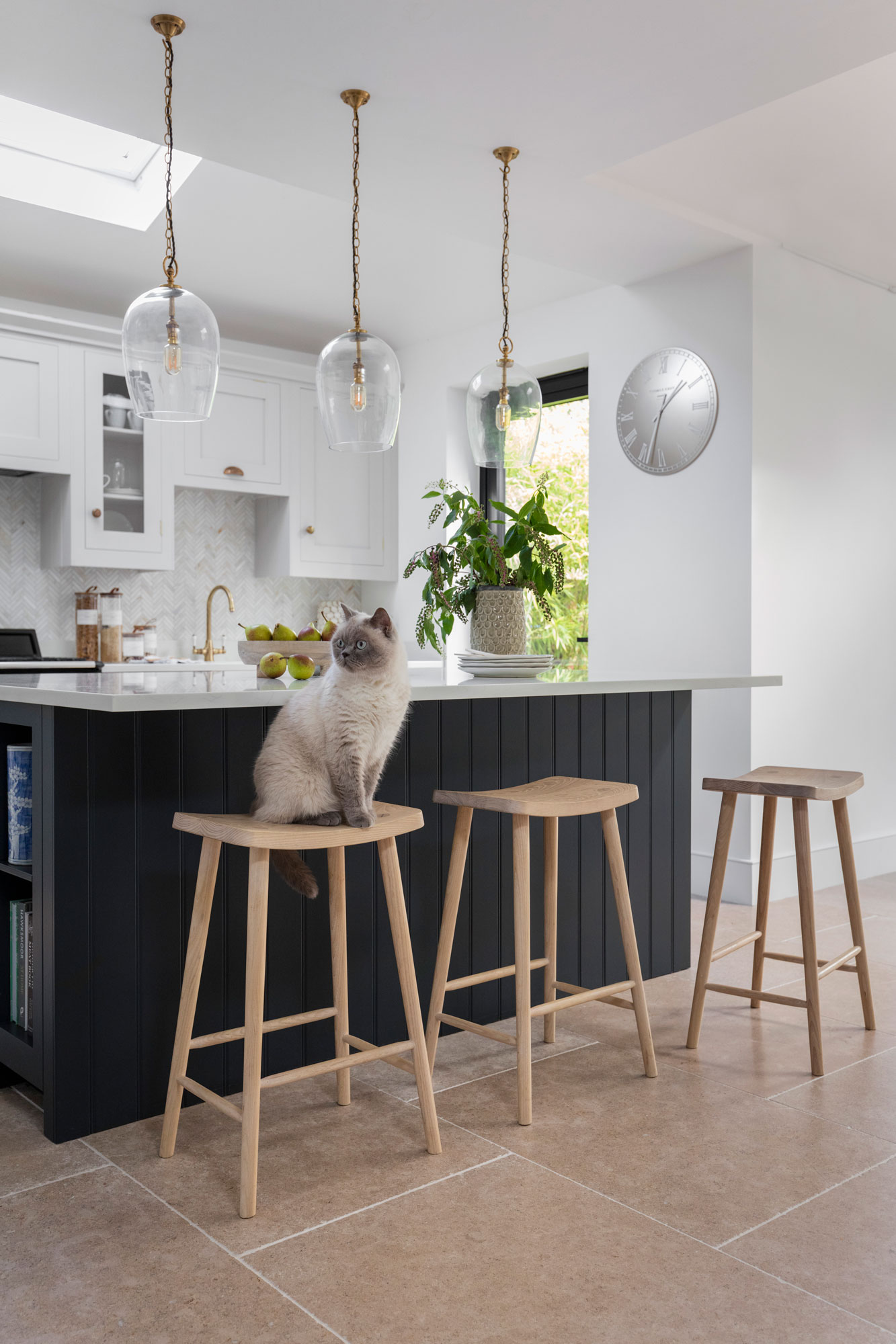 Dark Shaker kitchen island with white worktop and cream and black stools overlooking white Shaker kitchen cabinetry
