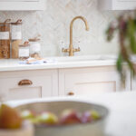 White Shaker kitchen cabinetry with brass handles and white worktop with brass tap against herringbone tiled splashback