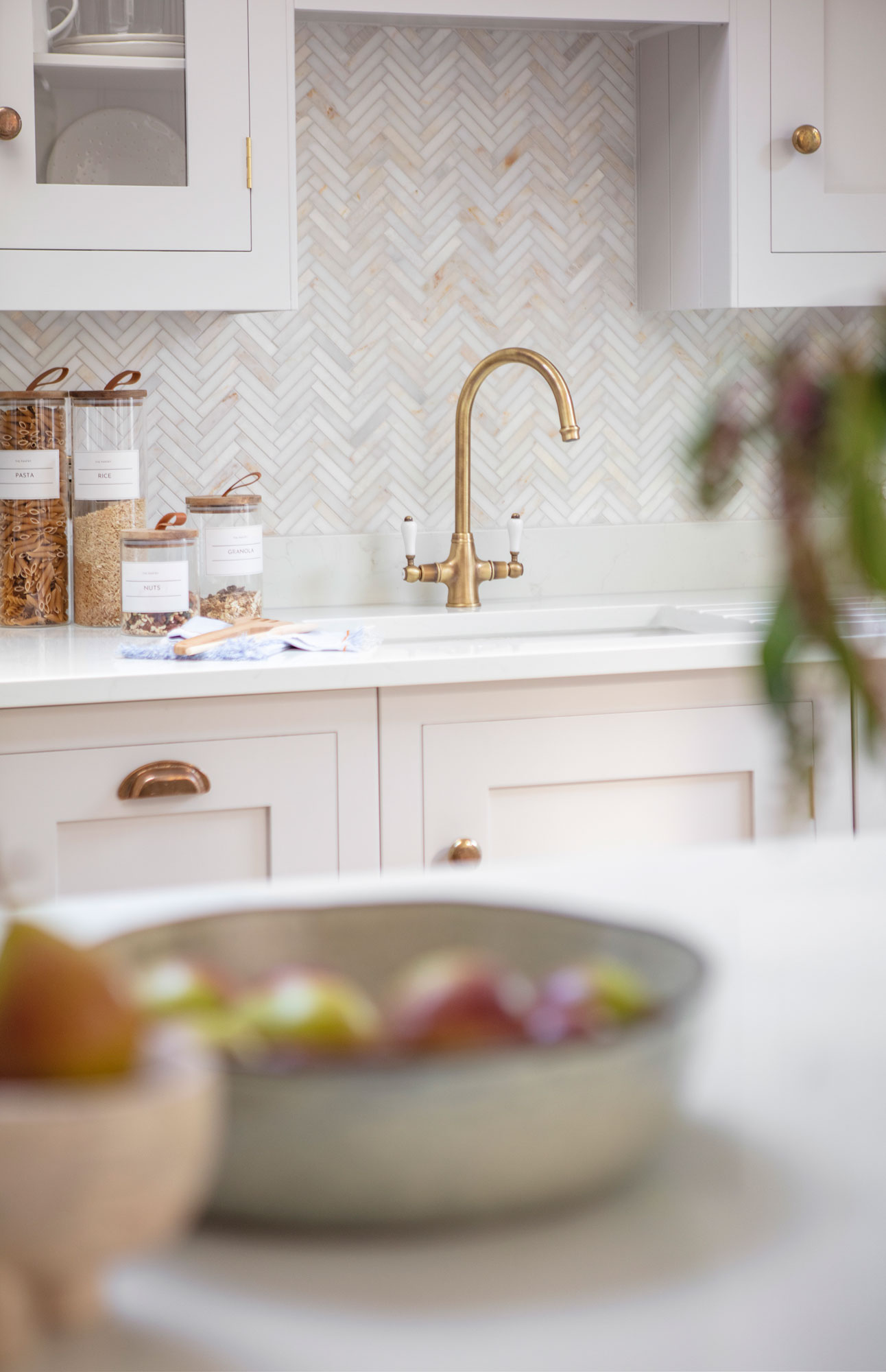 White Shaker kitchen cabinetry with brass handles and white worktop with brass tap against herringbone tiled splashback