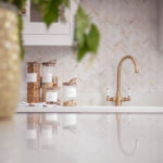 Beige herringbone tiled splashback against white worktop with integrated sink and brass tap