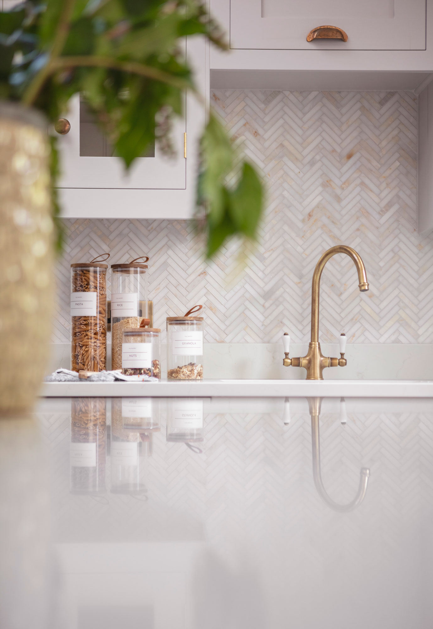 Beige herringbone tiled splashback against white worktop with integrated sink and brass tap