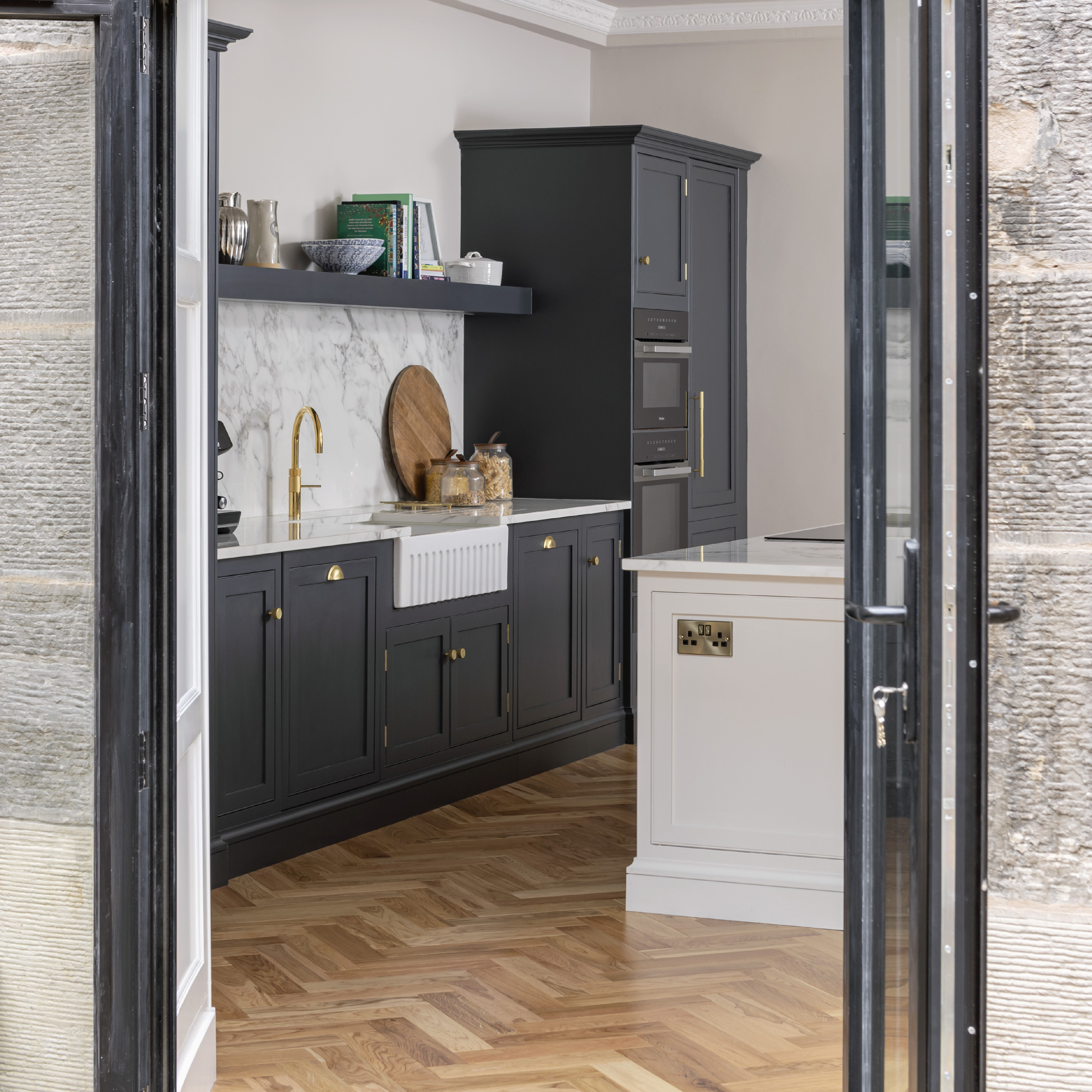 Dark Arbor kitchen cabinetry next to a beige kitchen island viewed from open French doors