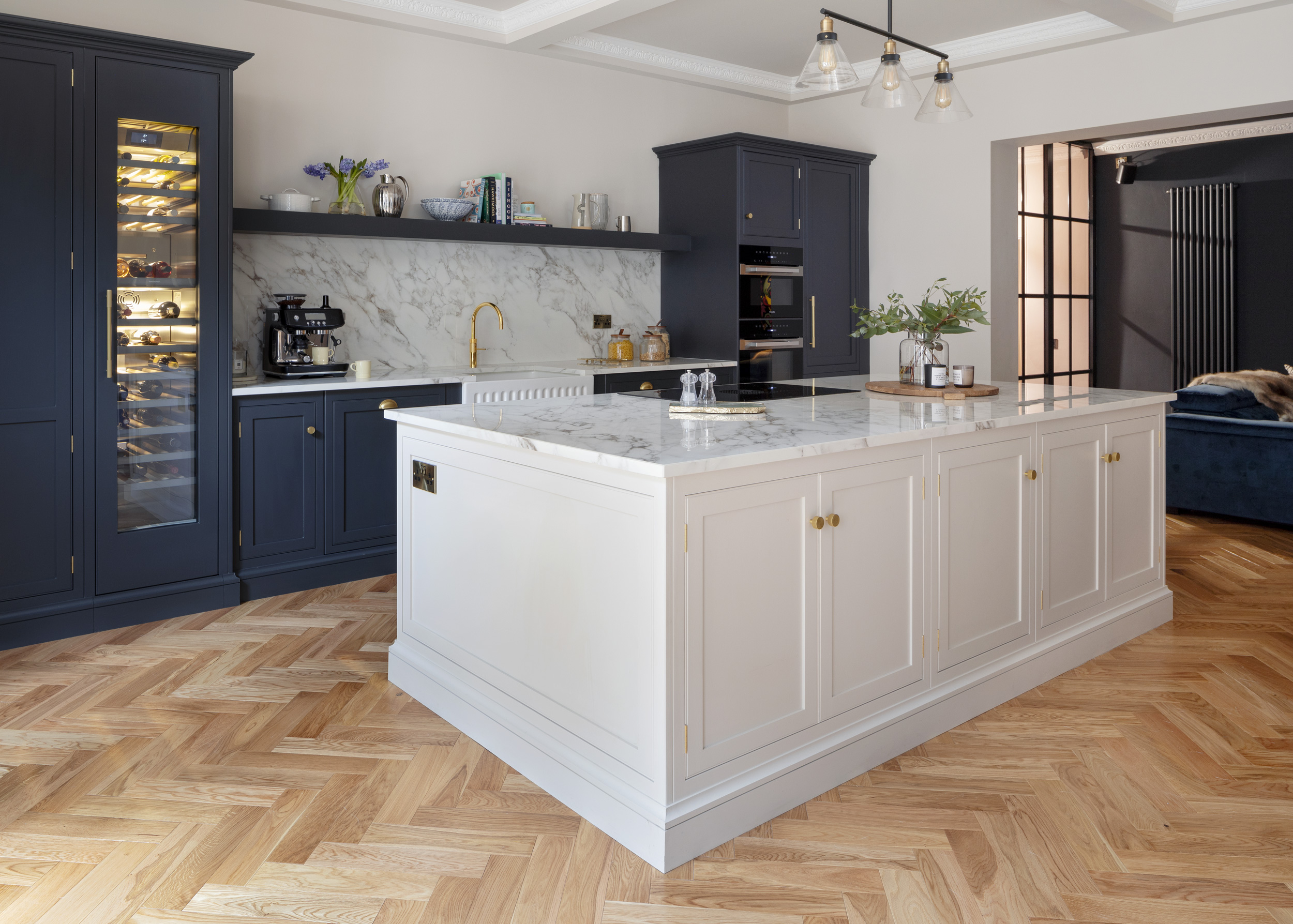 Beige kitchen island in front of dark Arbor cabinetry featuring white marble worktops