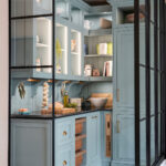 Full view of luxury walk-in pantry with open shelving, accent lighting, and classic blue cabinets with drawer storage.