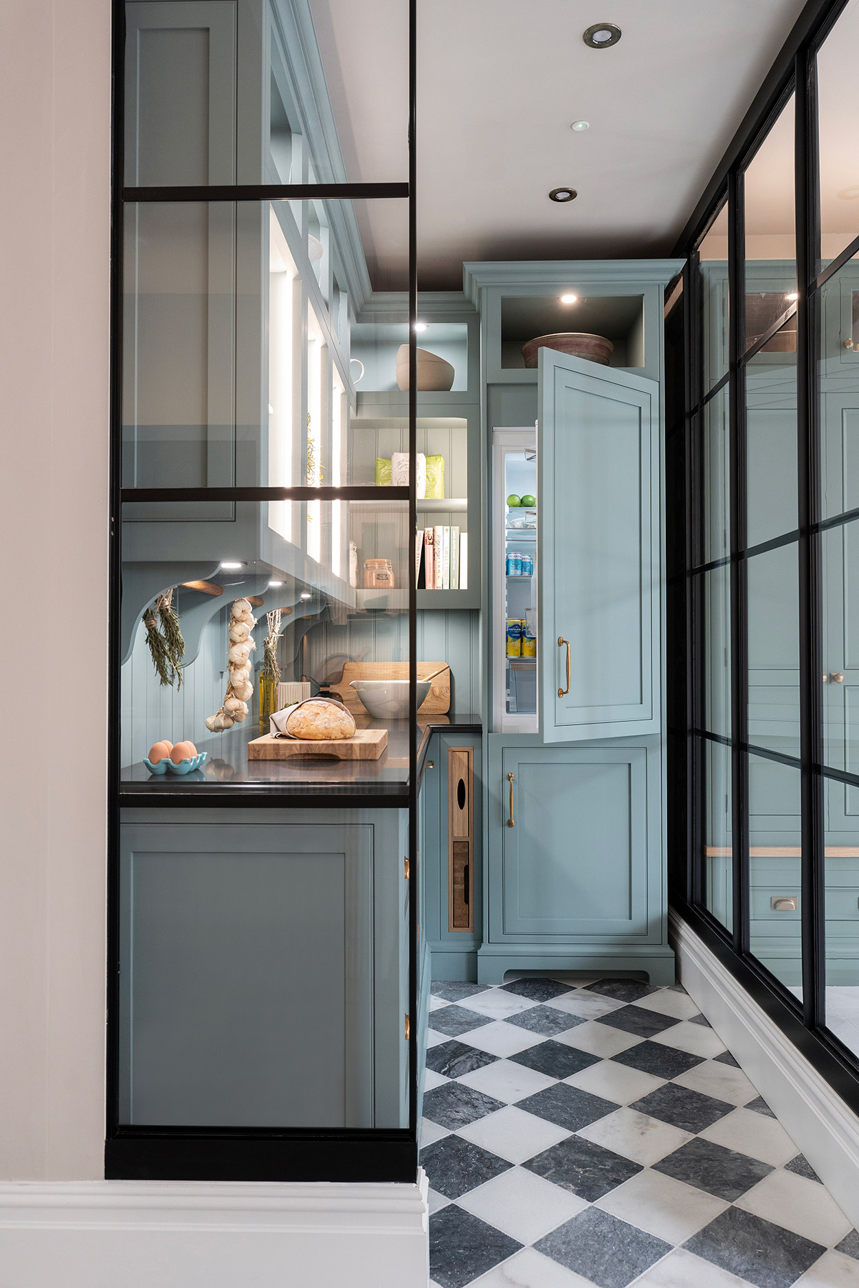 Elegant walk-in pantry design with checkered flooring, pale blue cabinetry, and integrated fridge, blending classic styling with modern kitchen luxury.