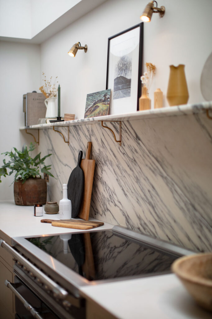 Scandi style kitchen with open shelving above cooking zone displaying artwork, plants, books and ceramics
