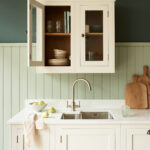 Hampton white kitchen cabinetry with white worktop and organised cupboard, featuring pale green wooden wall cladding