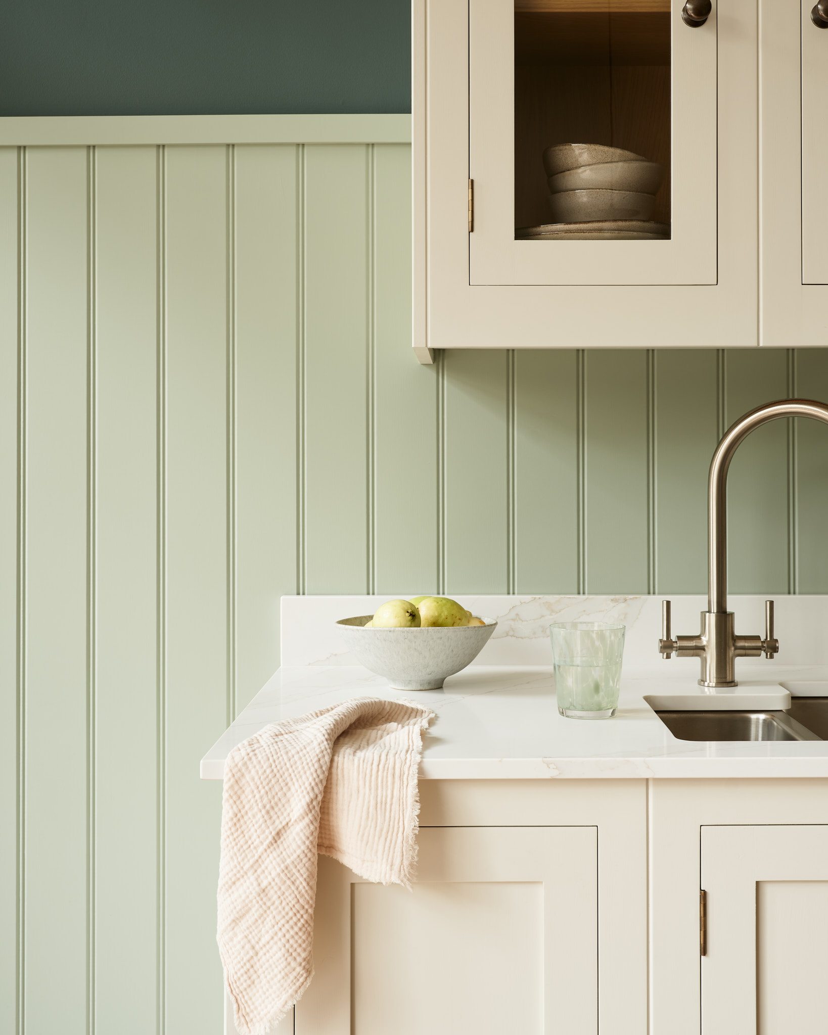 Hampton white kitchen cabinetry and white worktop with silver sink featuring pale green wooden wall cladding