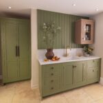 Sage green kitchen cabinetry with white worktop and splashback and white sink with gold tap