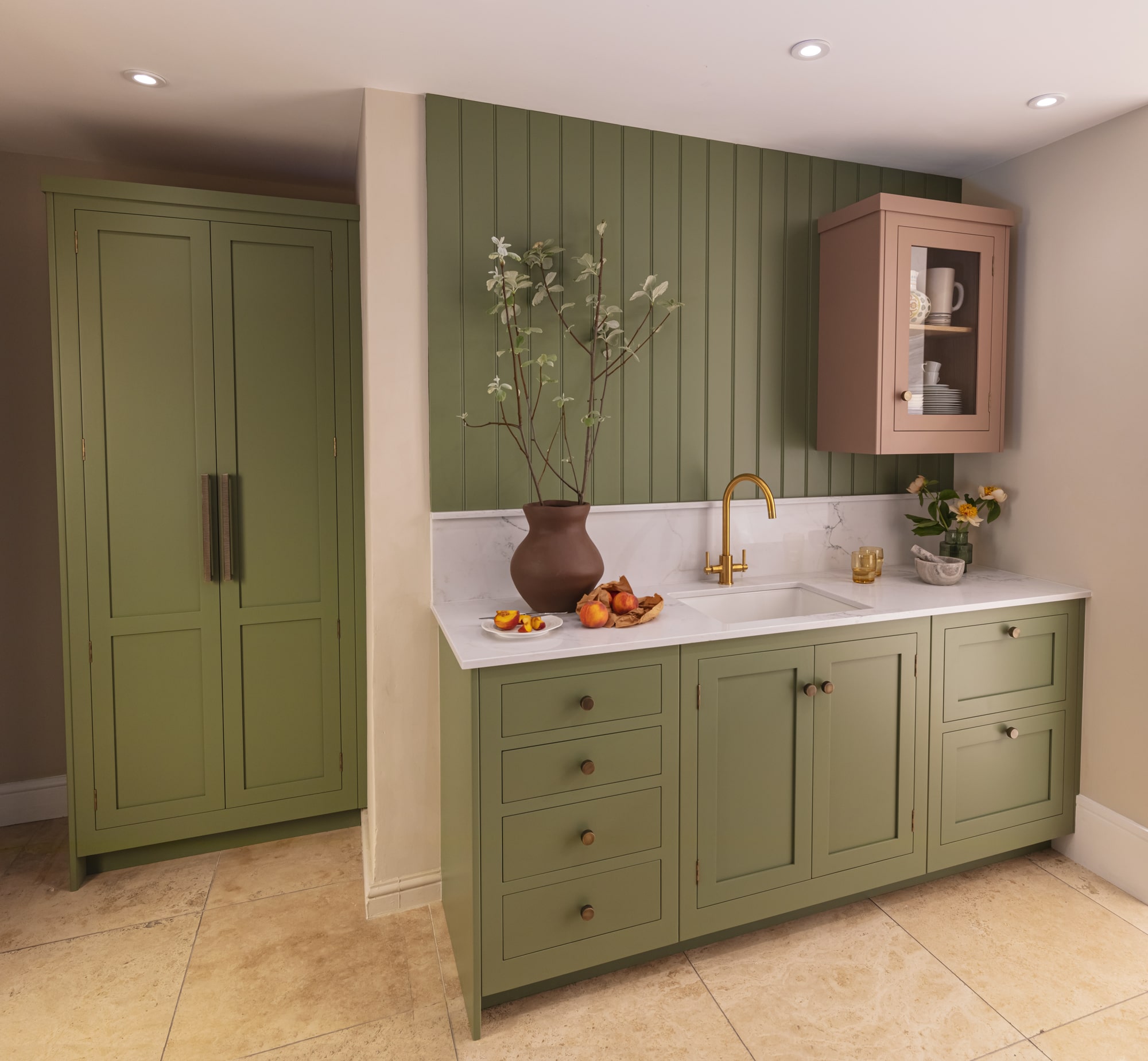 Sage green kitchen cabinetry with white worktop and splashback and white sink with gold tap