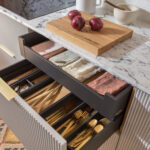 Grey reeded kitchen cupboard drawers open to black wooden cutlery dividers