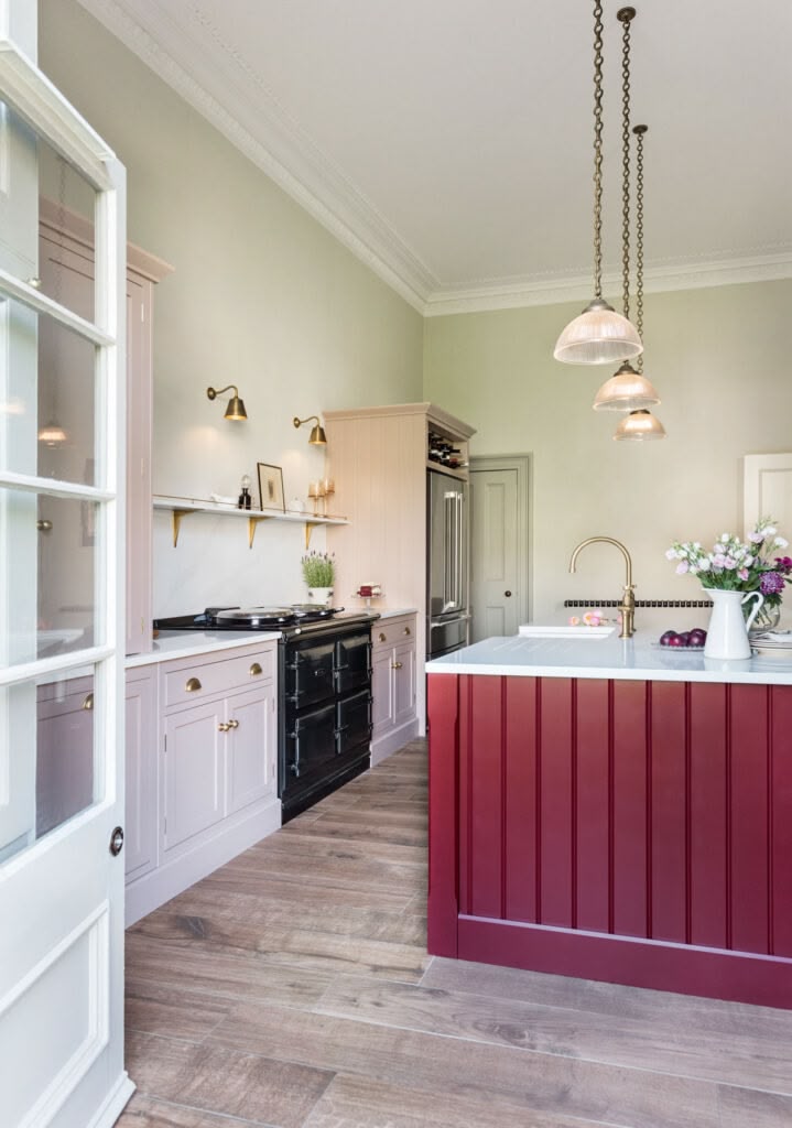 Burgundy kitchen island and blush pink cabinetry with white worktops against pale green walls