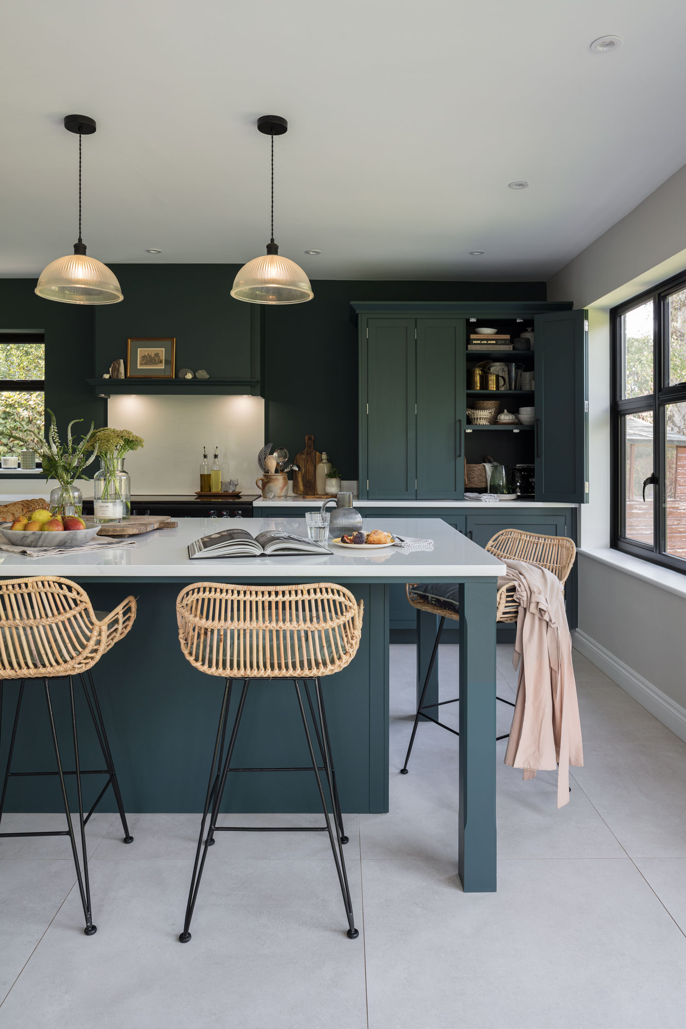 Dark green kitchen island with white worktop featuring weaved bar stools