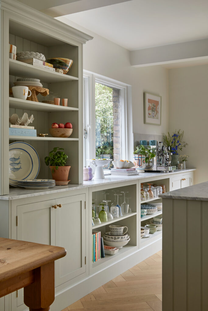 Light green kitchen with built in dresser featuring open storage displaying glassware and ceramics