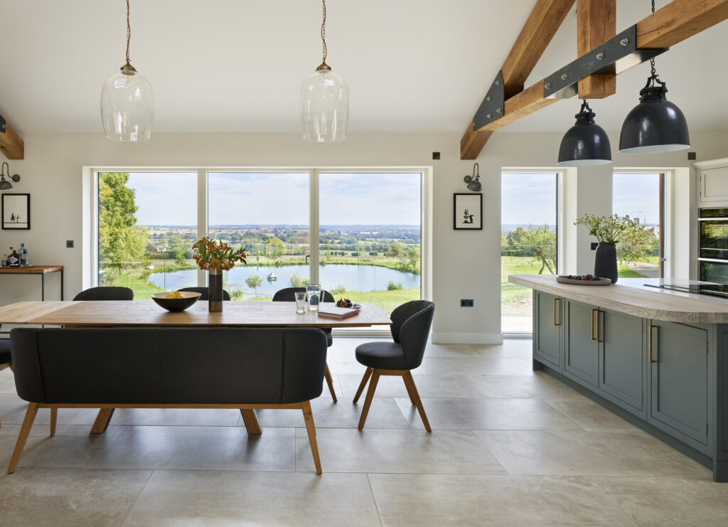 Spacious kitchen-dining area with curved edges and a nature inspired palette. Featuring large windows, overlooking a scenic outdoor view.