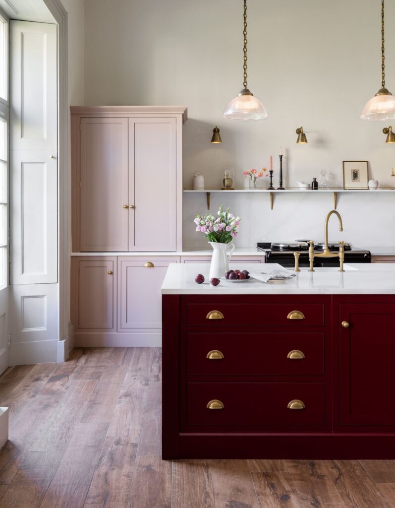 A stylish and timeless kitchen showcasing a vibrant red island, light pink cabinetry and luxurious gold fixtures.