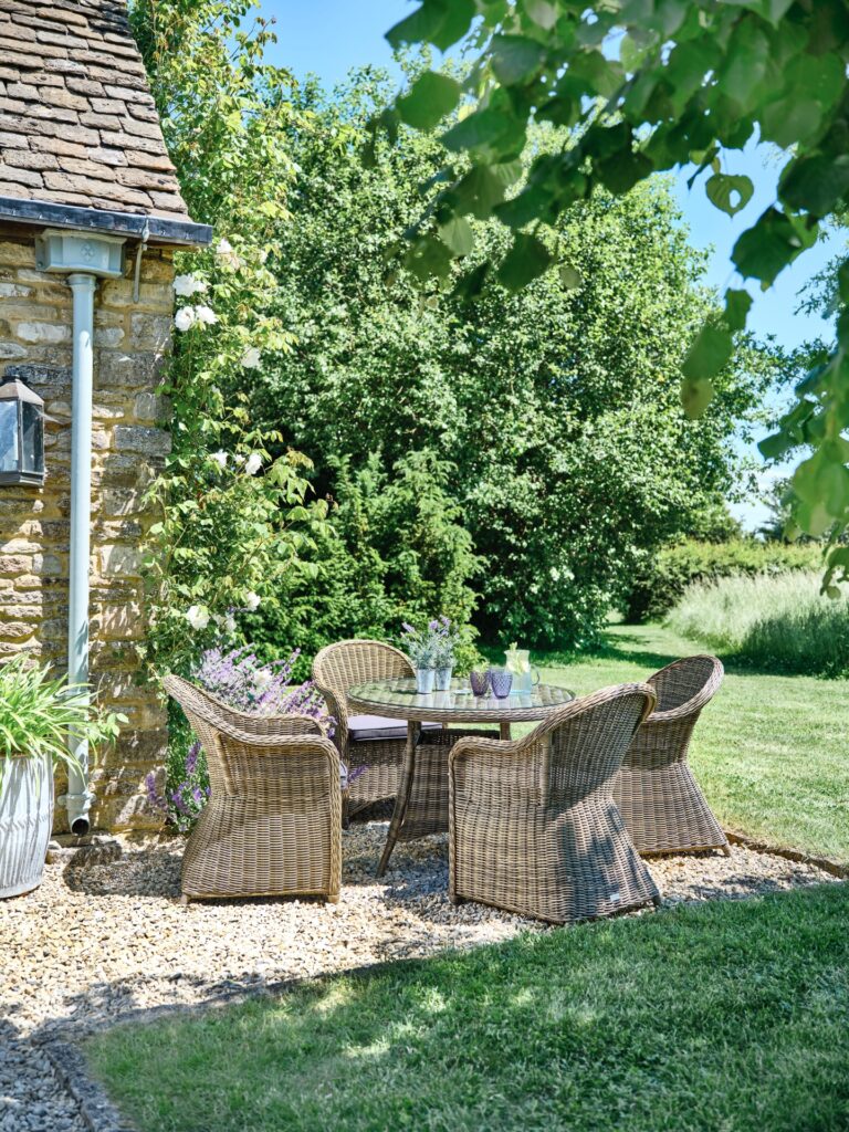 Sunny garden with wicker chairs around a dining table.