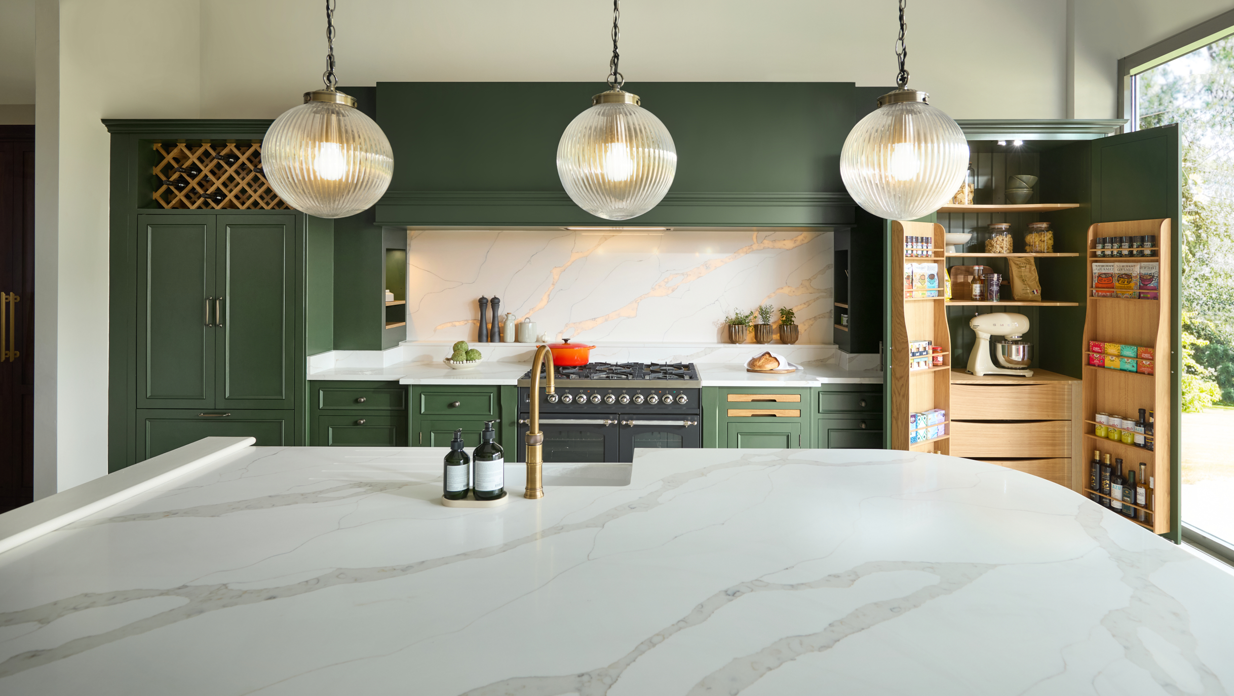 Green Kitchen with pendant lights sweeping over the island with pantry doors open to the right