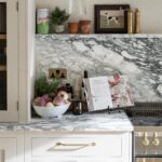 Modern kitchen countertop featuring a marble surface with a basket of fresh vegetables, cooking books propped open, and decorative items.