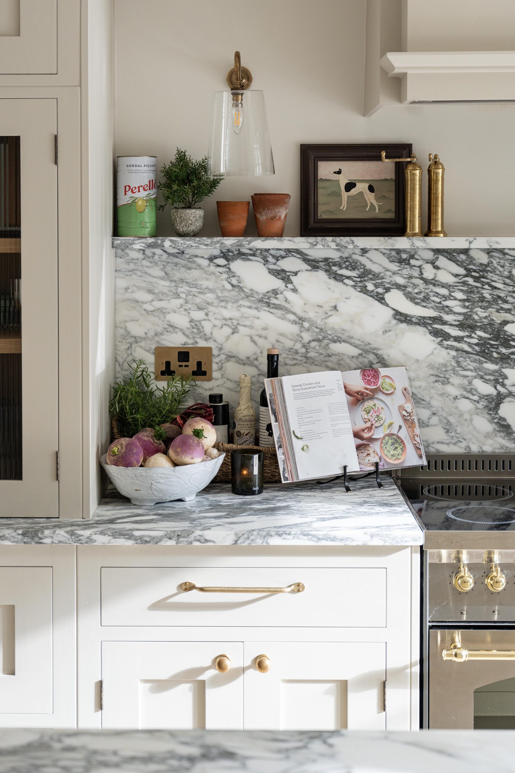 Modern kitchen countertop featuring a marble surface with a basket of fresh vegetables, cooking books propped open, and decorative items.