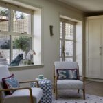 Interior view of a cosy nook with two armchairs and a side table, positioned by a window with a garden view. Decor includes patterned cushions, a small rug, and tasteful ornaments on the window sill.