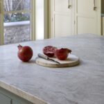 Pomegranates resting on a wooden cutting board placed on a marble worktop of a blue kitchen island. In the background, bright yellow cabinetry adds a colourful and modern touch to the kitchen.