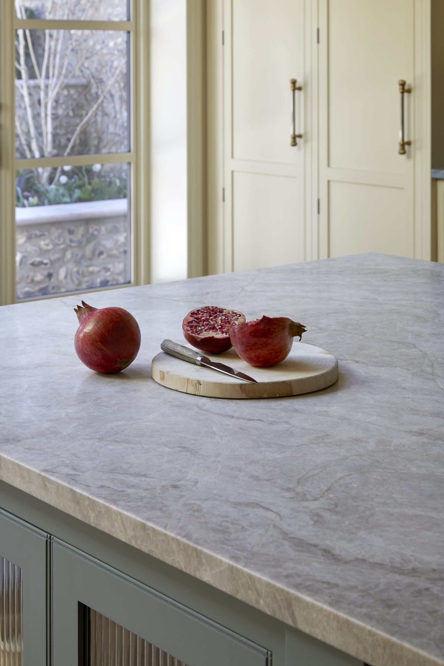 Pomegranates resting on a wooden cutting board placed on a marble worktop of a blue kitchen island. In the background, bright yellow cabinetry adds a colourful and modern touch to the kitchen.