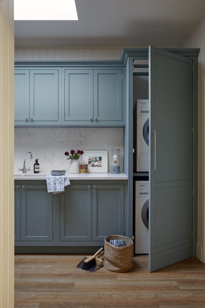 A tidy utility room featuring blue cabinets, a stacked washing machine and dryer, a small sink, and a wicker basket with a pair of shoes beside it.