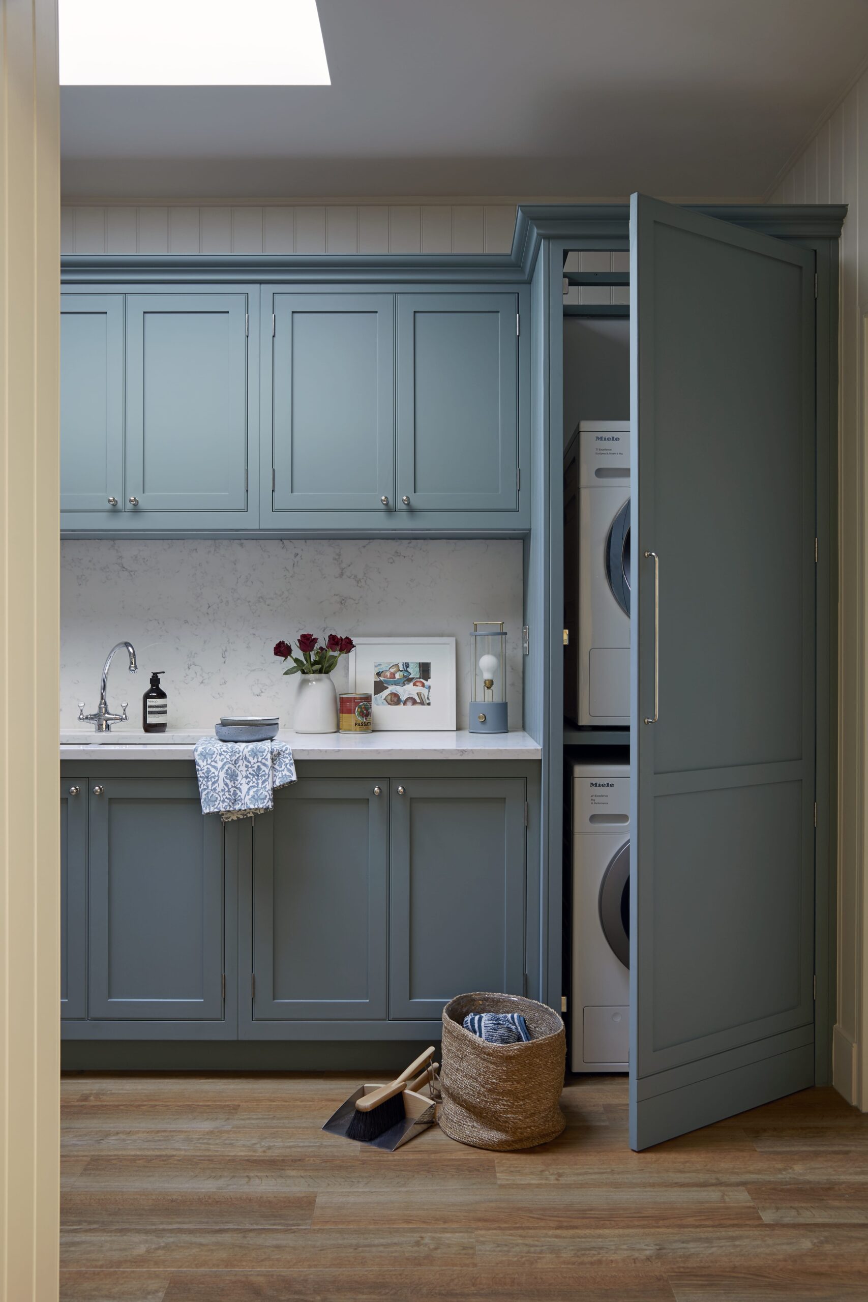 A tidy utility room featuring blue cabinets, a stacked washing machine and dryer, a small sink, and a wicker basket with a pair of shoes beside it.
