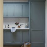 A tidy utility room featuring blue cabinets, a small sink, and a wicker basket with a pair of shoes beside it.