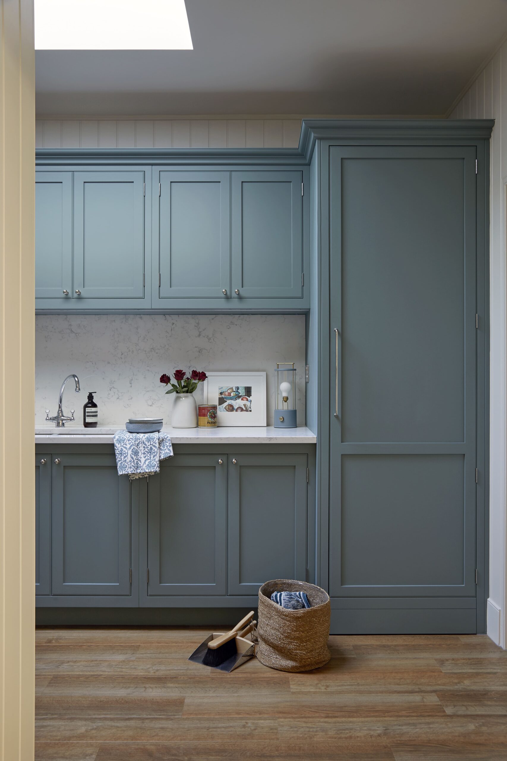 A tidy utility room featuring blue cabinets, a small sink, and a wicker basket with a pair of shoes beside it.