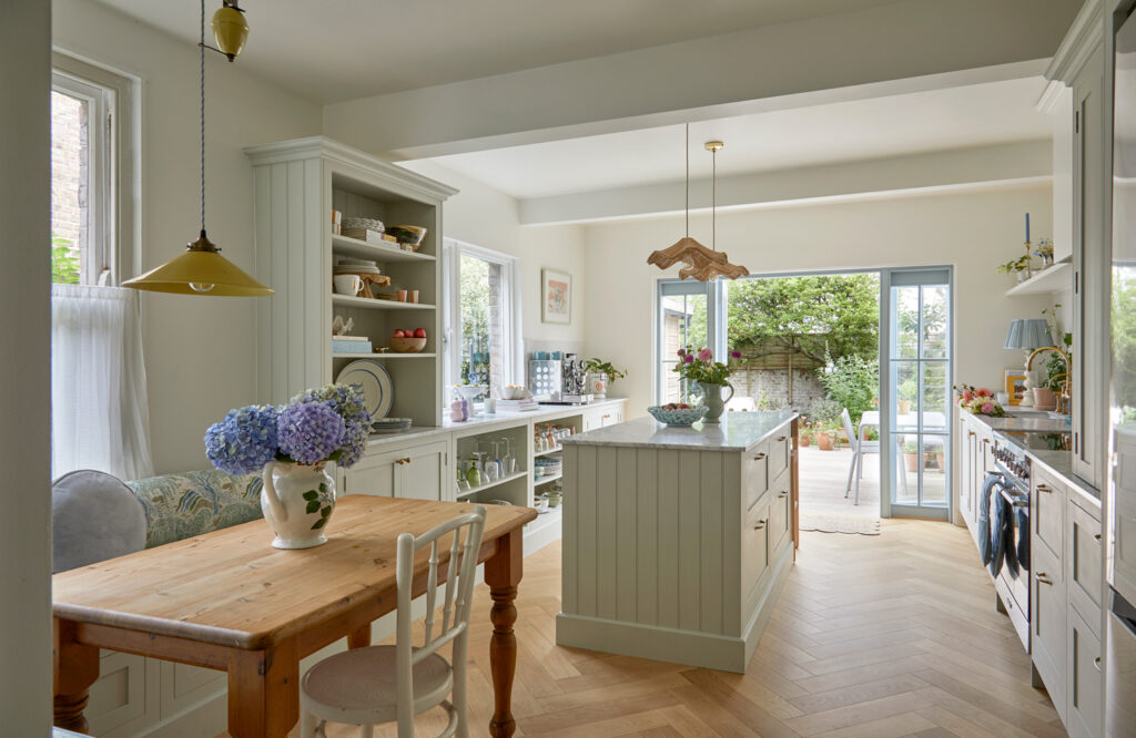 A sage green family kitchen, bespoke kitchen, kitchen island, open plan living displays sage green family kitchen, bespoke kitchen, kitchen island, and open plan living come together in a harmonious design. the focal point is a stunning kitchen island, where natural wood meets sleek white, adorned with a blue and white floral touch. the open plan seamlessly integrates the kitchen with living space, inviting relaxation and family gatherings. the sliding glass door to the patio adds a touch of tranquility, creating a truly unique and inviting oasis.