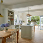 A sage green family kitchen, bespoke kitchen, kitchen island, open plan living displays sage green family kitchen, bespoke kitchen, kitchen island, and open plan living come together in a harmonious design. the focal point is a stunning kitchen island, where natural wood meets sleek white, adorned with a blue and white floral touch. the open plan seamlessly integrates the kitchen with living space, inviting relaxation and family gatherings. the sliding glass door to the patio adds a touch of tranquility, creating a truly unique and inviting oasis.