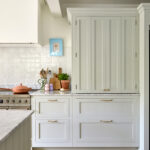 A luxury sage green kitchen, hidden kitchen storage displays seamless integration, with elegantly concealed storage compartments. White cabinets and gold accents provide a sleek touch, while the countertops light beige complements them perfectly. The well-thought-out design adds a hint of sophistication and functionality, creating a space that seamlessly blends modernity and tradition.