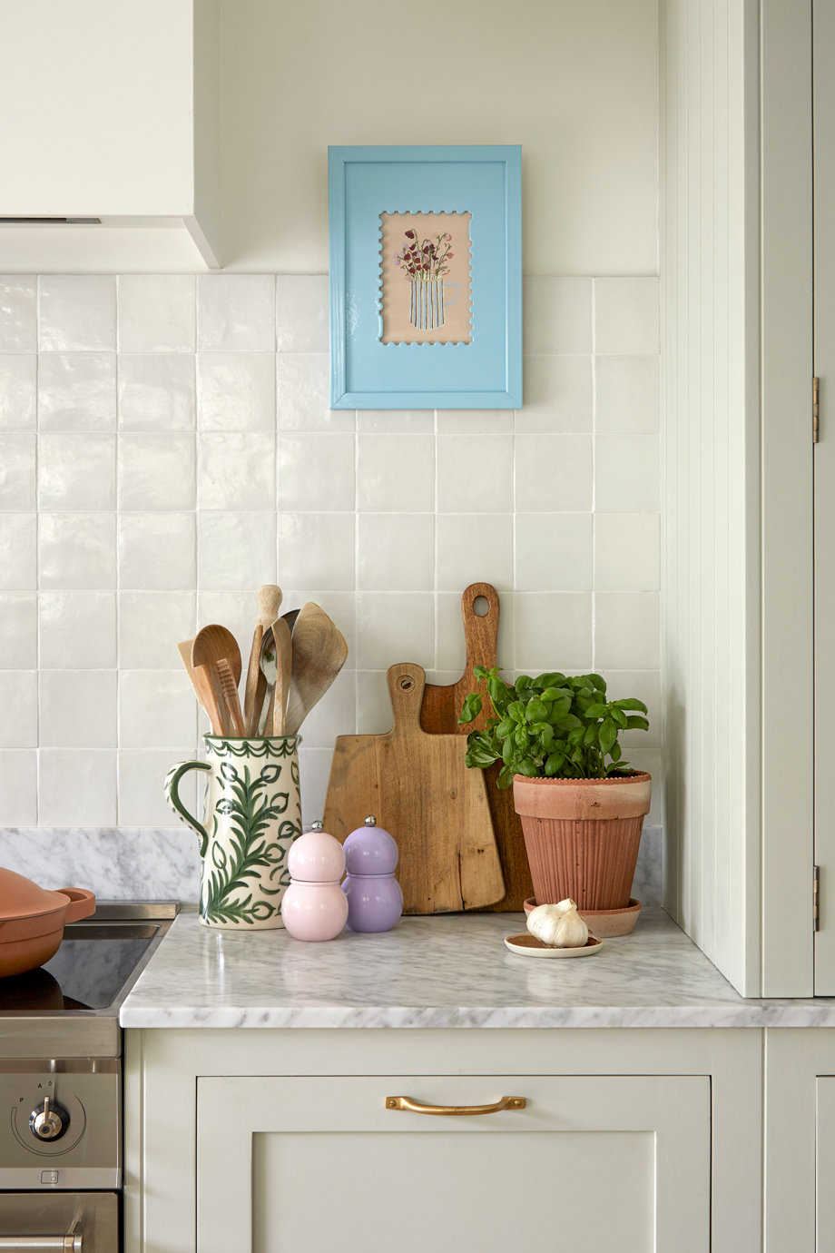 A bespoke kitchen, personalisation displays a carefully curated countertop, where a wooden bowl, matching chopping and cutting boards, and a floral mug create a harmonious blend of nature and craftsmanship. The white tiles and blue picture frame reflect a unique touch, turning this space into a warm and inviting oasis for every cook.