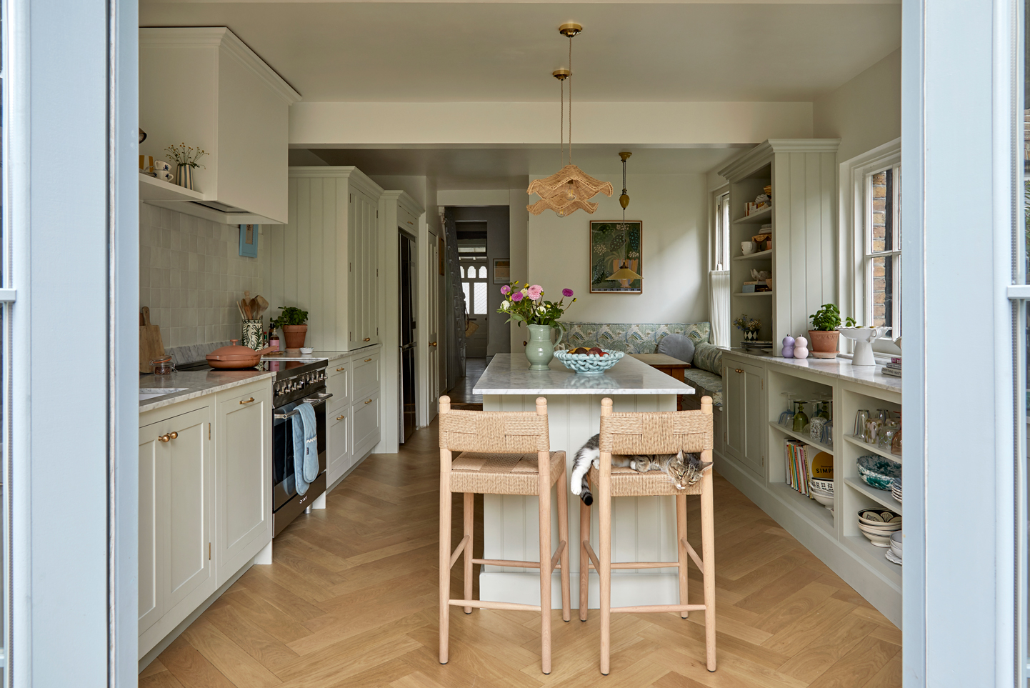 A indoor outdoor kitchen, kitchen island displays a harmonious blend of modernity and rusticity. The island, with its white marble and wooden countertop, centerpiece, holds a blue vase and a green plant, creating a serene atmosphere. Equipped with a silver stove and microwave, the island is flanked by sleek white cabinets and a refrigerator, while a wooden bar and stool add warmth. This unique fusion of elegance and charm defines the space.