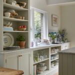 A kitchen storage, sage green kitchen displays a meticulously organized area, with cabinets in harmonious white and sage. Decorative blue and white accents complement the space, creating a visually appealing and well-designed storage solution.