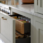 A kitchen storage displays sleek design, with white cabinets and open drawers offering efficient organization. The minimalist aesthetic is enhanced by wooden accents and a pop of color from a pink pot, creating a cozy and well-organized space.