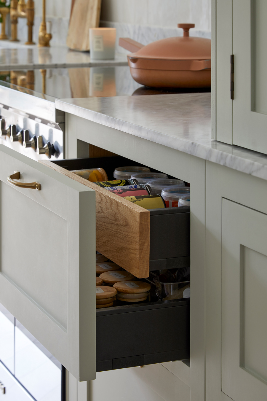 A kitchen storage displays sleek design, with white cabinets and open drawers offering efficient organization. The minimalist aesthetic is enhanced by wooden accents and a pop of color from a pink pot, creating a cozy and well-organized space.