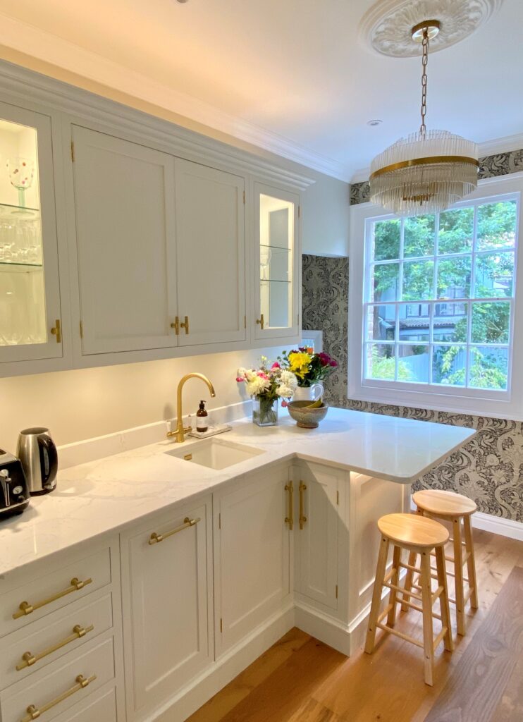 A small kitchen featuring white cabinets, gold accents, integrated seating, and ample storage space.